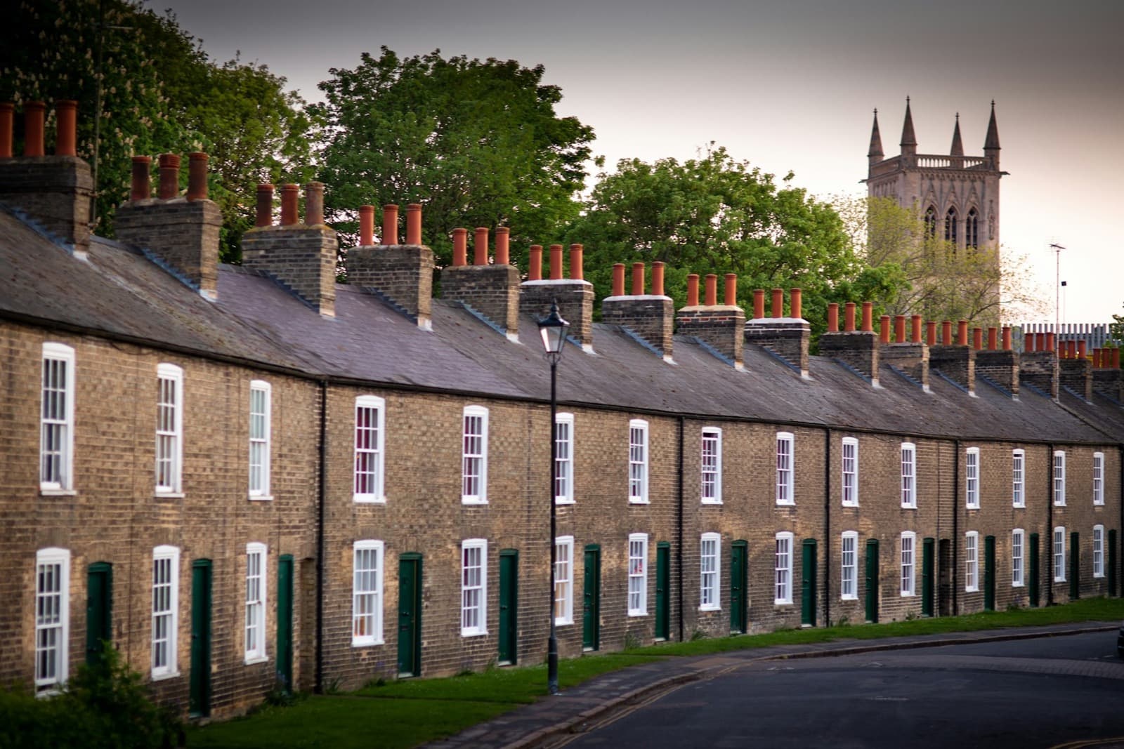 A terrace of brick cottages with green shutters and tall chimneys, a church tower behind