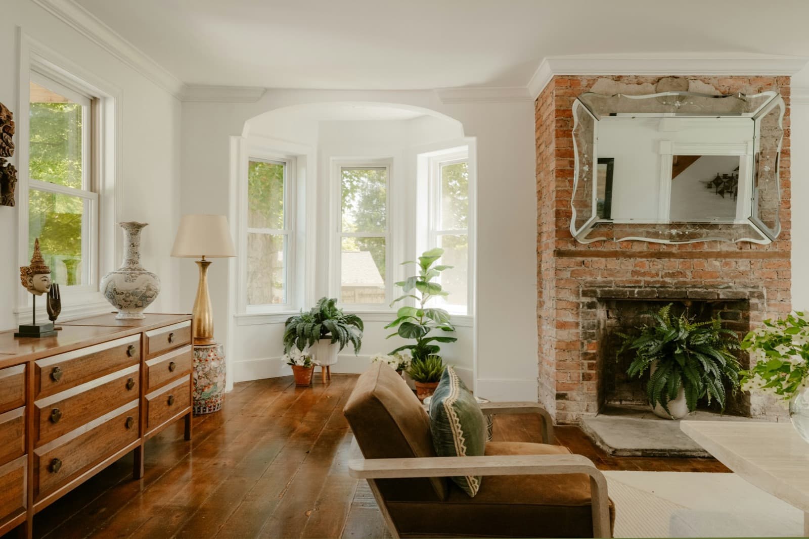 A sitting room with a bare-brick fireplace, a bay window and a wooden floor