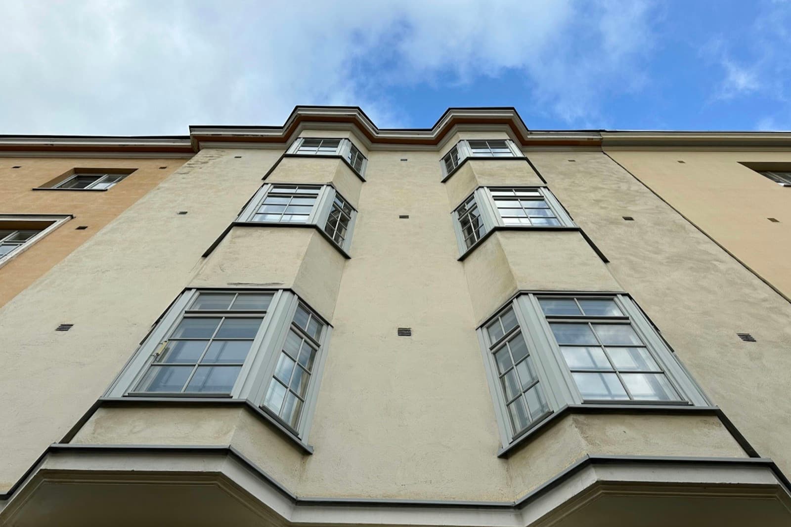 Looking up a rendered flat facade with tiered bay windows against a blue sky
