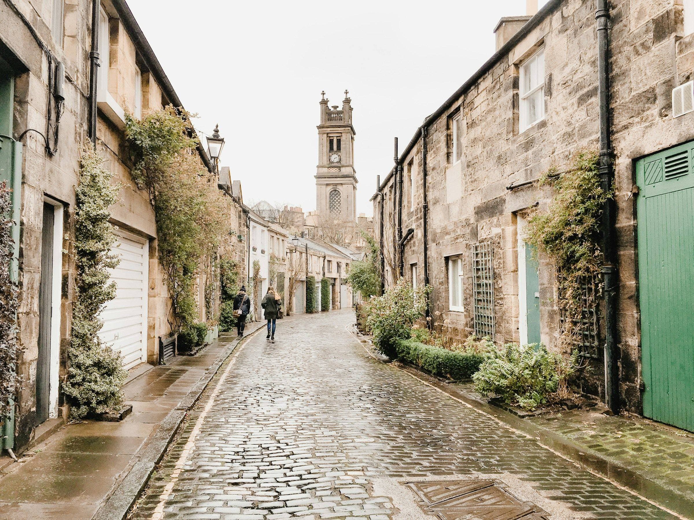 Wet cobbles and mews houses on Circus Lane in Stockbridge, with St Stephen's clock tower behind