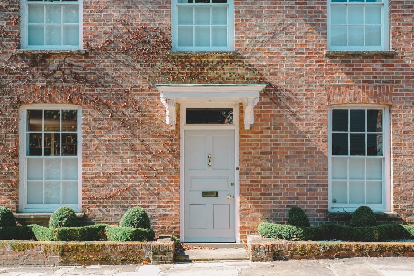 Brick house frontage with a pale blue front door and clipped hedges