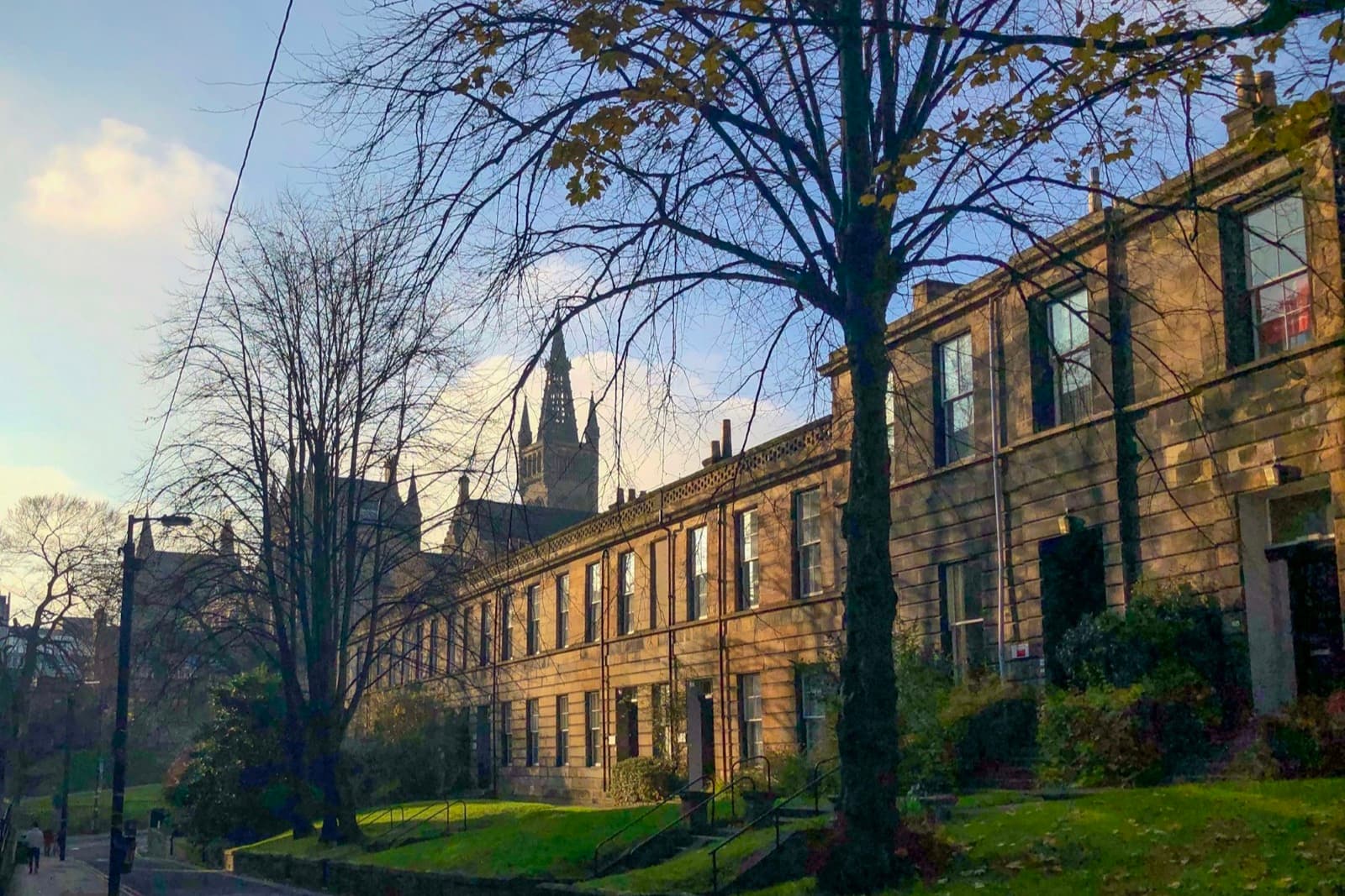Sandstone tenement terrace in low sun, with a church spire behind